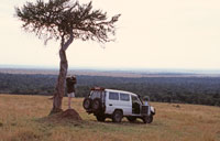 A Paul Augustinus image of a vehicle parked on the slope of an escarpment in the Mara Reserve, with the plains in the background.